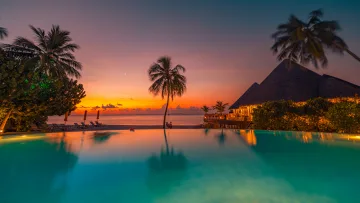 beach, luxury, resort, sunset - Una lussuosa piscina a sfioro riflette un vibrante tramonto arancione e viola sopra una spiaggia con palme e resort.