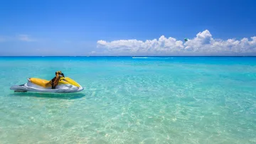activity, sea - A vibrant yellow jet ski floats on the calm turquoise ocean surface under a bright blue sky with scattered clouds.