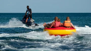 activity, sea - Persone che si divertono su un gommone trainato da una moto d'acqua sull'oceano blu in una soleggiata giornata estiva.