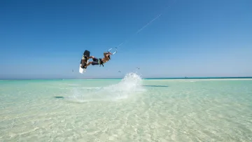 activity, sea - A professional kitesurfer performs a high jump above the crystal clear turquoise water on a sunny day in paradise.