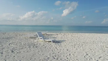 beach, local-island, relax - Empty white sunloungers on the pristine sandy beach of Felidhoo Island, Vaavu Atoll, under a bright blue sky.