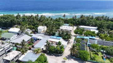 drone-shot, local-island - Drone perspective of Fulhadhoo Island in the Baa Atoll, showing residential buildings, lush palm trees, and the beach.