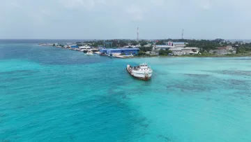 local-island, sea - Aerial view of a boat in the turquoise lagoon of Hinmafushi island, Kaafu Atoll, with the industrial harbor area.