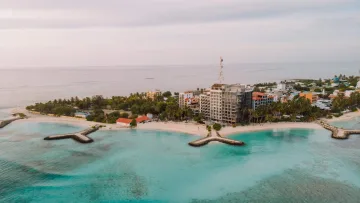 Drone perspective of Maafushi local island in Kaafu Atoll featuring sandy beaches, lush palm trees, and coastal buildings.