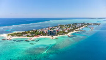 Aerial drone shot of Maafushi local island in Kaafu Atoll, featuring turquoise waters, sandy beaches, and buildings.