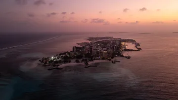 drone-shot, local-island, sky, sunset - Drone view of Maafushi local island in Kaafu Atoll, Maldives at sunset with glowing lights and calm ocean waters.