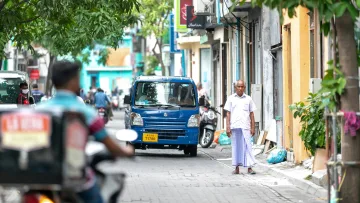 culture, local-island, people - Un uomo anziano con indosso un sarong tradizionale cammina lungo una stretta via di Male, Atollo di Kaafu, con un furgone.