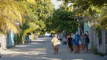 local-island, people - A group of tourists walking barefoot on a sandy road surrounded by lush tropical vegetation on Omadhoo, Alifu Dhaalu.