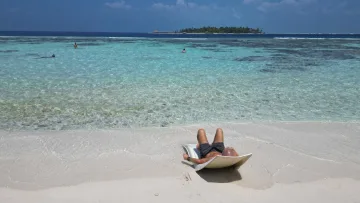 Uomo che prende il sole su un lettino alla spiaggia di Thinadhoo nell'atollo di Vaavu con persone che nuotano in mare