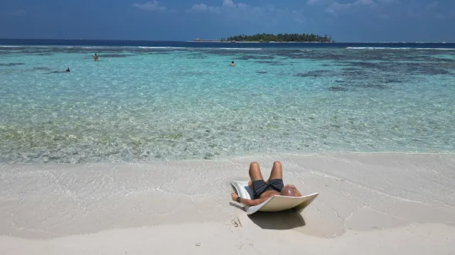 beach, bikini-beach, local-island, people, relax, sea - Man sunbathing on a white lounger at Thinadhoo local island beach in Vaavu Atoll with people swimming in clear sea