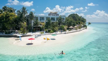 Veduta aerea della spiaggia sull'isola locale di Thinadhoo nell'atollo di Vaavu, con hotel, palme e acqua cristallina.