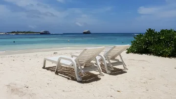 beach, bikini-beach, local-island, sea - Due sdraio bianche sulla spiaggia di sabbia dell'isola locale di Thulusdhoo, atollo di Kaafu, con barche nell'oceano.