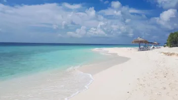 White sandy beach with thatched umbrellas at Ukulhas local island in Alifu Alifu Atoll under a bright blue sky.