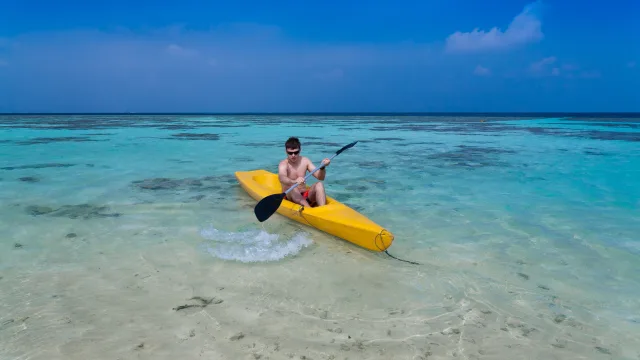 activity, sea - Un giovane con occhiali da sole che pagaia su un kayak giallo attraverso le acque turchesi basse e trasparenti di una laguna tropicale.