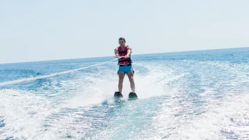 activity - A man wearing a life jacket is water skiing behind a boat, gliding over the sparkling blue ocean surface.