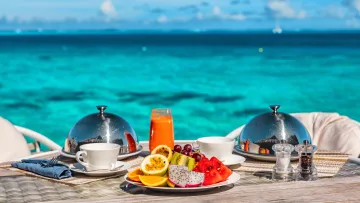 food, luxury, resort, sea - Un tavolo da colazione di lusso con frutta fresca tropicale e bevande su uno sfondo spettacolare di mare turchese.