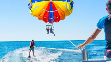 activity, sky - A couple soaring in the sky with a colorful parasailing canopy towed by a boat over the clear blue ocean waters