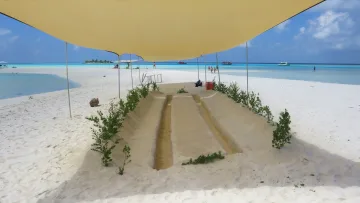 activity, beach, relax - A romantic sand-sculpted dining table set on a white sandbank beach under a beige canopy with turquoise sea views.