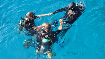 activity - Aerial view of three scuba divers in full gear holding hands while floating in the clear blue tropical ocean water.
