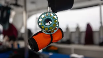 activity - Close up of a bright orange scuba diving surface marker buoy and finger spool hanging on a boat deck.