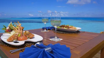 food, luxury, resort, sea - Due bicchieri di vino bianco e piatti di frutti di mare serviti su un tavolo di legno con un bellissimo mare blu sullo sfondo.