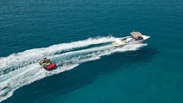 activity, drone-shot, sea - Vista aerea di un motoscafo che traina due persone su un gommone gonfiabile attraverso l'azzurro oceano tropicale.