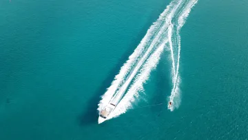 activity, drone-shot, sea - An aerial drone view of a white speedboat pulling a person waterskiing across the turquoise blue ocean waters.