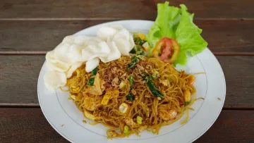 food - A plate of delicious stir-fried vermicelli noodles topped with prawn crackers and fresh lettuce on wooden table.