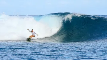 activity, people, sea - A female surfer riding a powerful, curling blue ocean wave under a bright sky in the tropical Maldives waters.