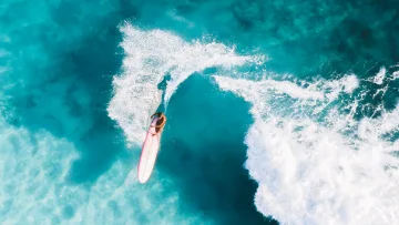 activity, drone-shot, sea - A drone shot capturing a surfer on a longboard carving through a vibrant turquoise wave with white foam cresting