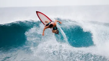 activity, sea - A professional surfer balancing on a red and white surfboard, carving through a powerful, turquoise ocean wave.