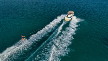 activity, drone-shot, sea - Aerial view of a woman water skiing behind a motorboat in deep blue tropical waters during a bright sunny day