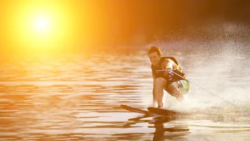activity, sunset - A young man enjoying water skiing on the sea during a vibrant golden sunset, creating splashes in the water.