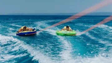 activity, sea - Due uomini si divertono cavalcando gonfiabili colorati trainati da una barca sopra le onde turchesi dell'oceano.