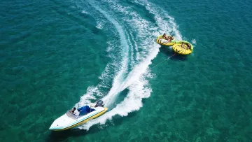 activity, people - Un motoscafo traina due ciambelle gonfiabili gialle con turisti felici attraverso il mare tropicale cristallino.