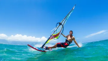 activity, people, sea, sky - Un uomo sorridente pratica windsurf su una tavola colorata attraverso l'oceano turchese sotto un cielo estivo azzurro.
