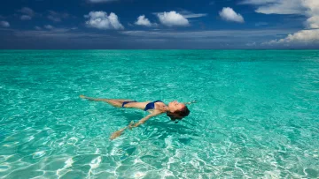 people, relax, sea - A woman in a blue bikini floats peacefully on her back in the calm, vibrant turquoise water under a blue sky.