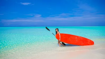 activity, people, sea - Una donna trasporta una tavola da stand up paddle arancione mentre cammina nell'acqua turchese cristallina.