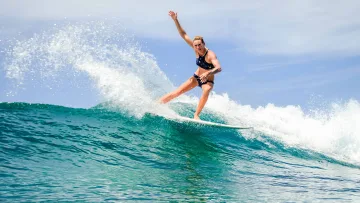 activity, sea - A fit woman surfing a turquoise ocean wave, performing a turn while balancing on her surfboard under a sunny sky.