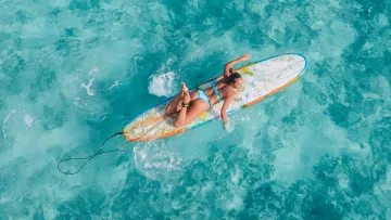 activity, drone-shot, people, sea - Aerial view of a woman paddling on a surfboard in crystal clear turquoise water during a tropical vacation.