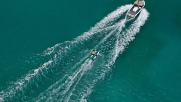 activity, drone-shot, sea - Aerial view from above of a woman in a yellow shirt water skiing pulled by a small speed boat across turquoise water