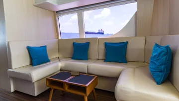facilities, luxury - Divano moderno in pelle bianca con cuscini blu all'interno di uno yacht di lusso vista oceano con nave mercantile.