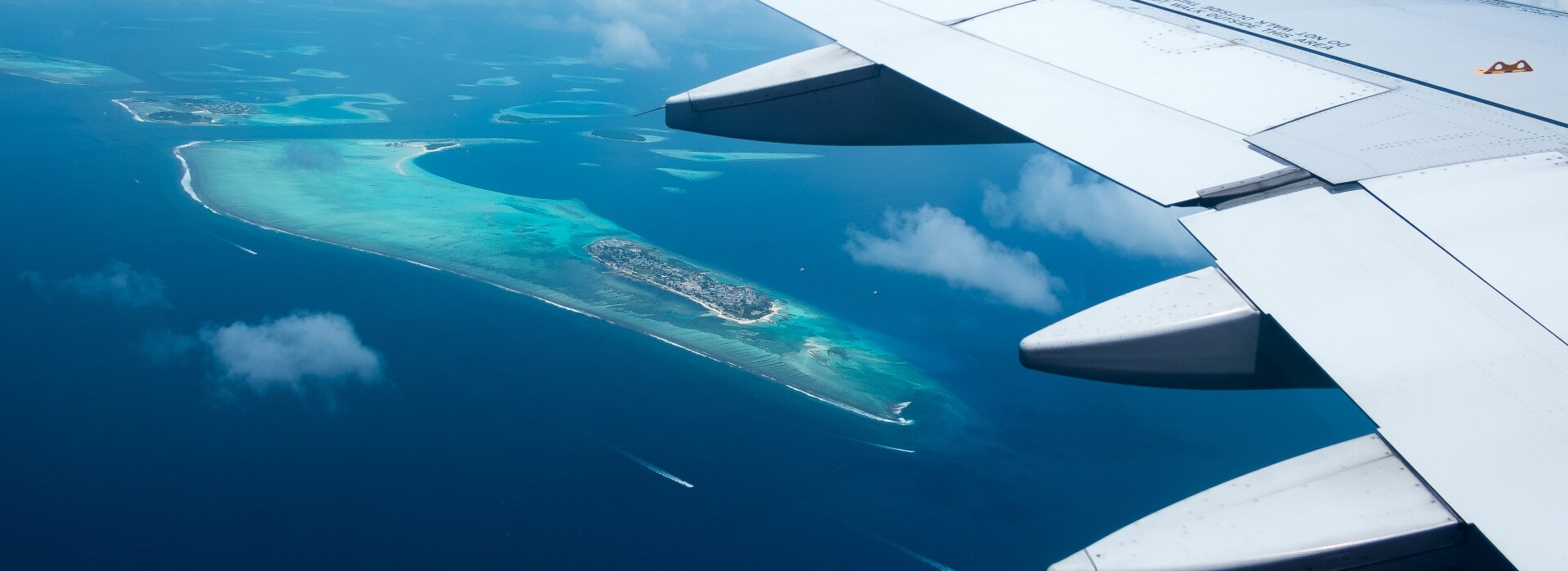 Stunning aerial perspective of turquoise coral islands and deep blue sea taken from an airplane wing in flight.
