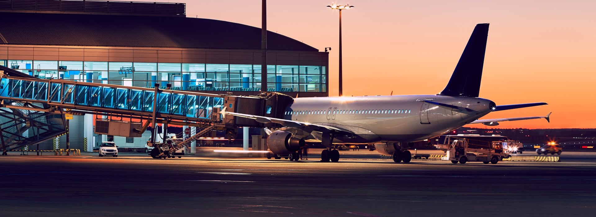 Commercial airplane parked at an airport boarding bridge during a beautiful golden hour sunset with terminal lights