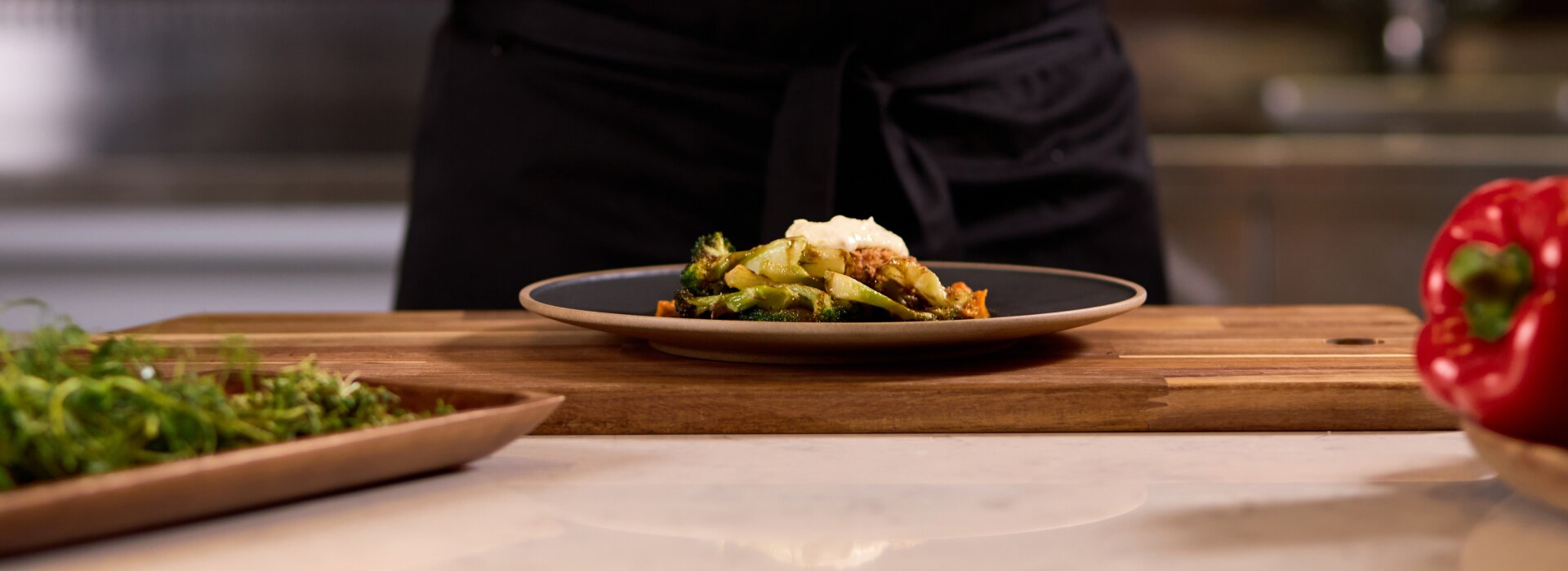 Uno chef professionista con divisa bianca usa un cucchiaio per impiattare con cura verdure saltate in una cucina di un ristorante.
