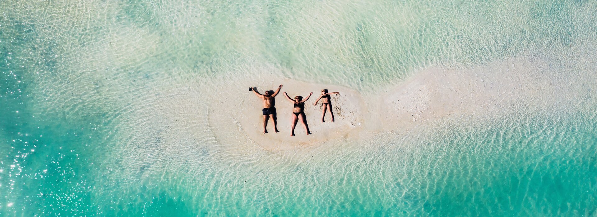Veduta aerea di una famiglia che si rilassa su una piccola lingua di sabbia bianca circondata da mare turchese.