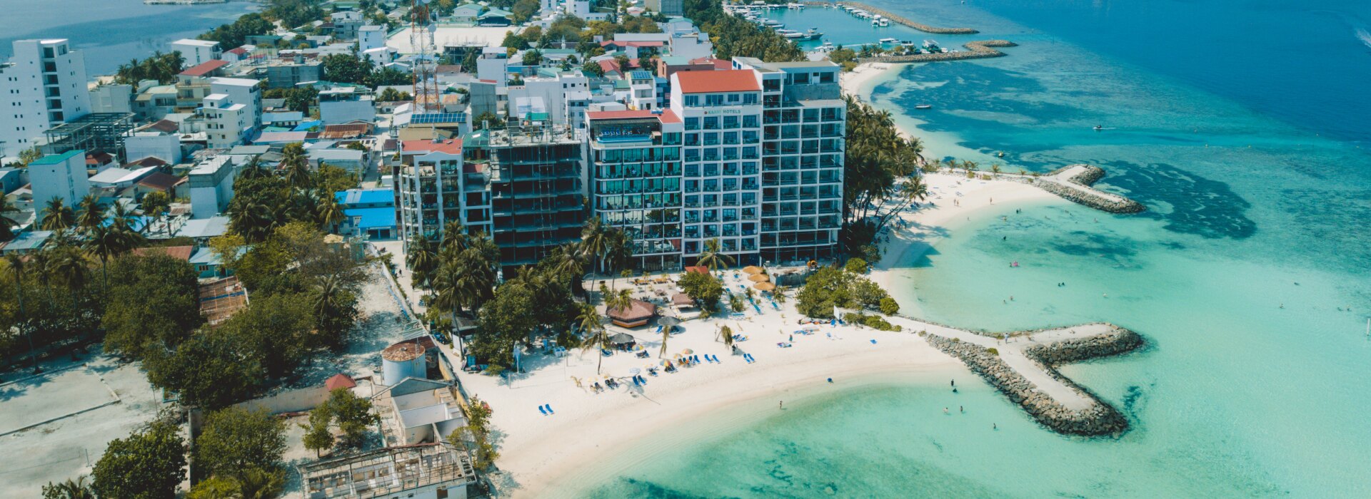 Aerial drone shot of Maafushi local island in Kaafu Atoll, showcasing its hotels, white beach and clear turquoise sea.
