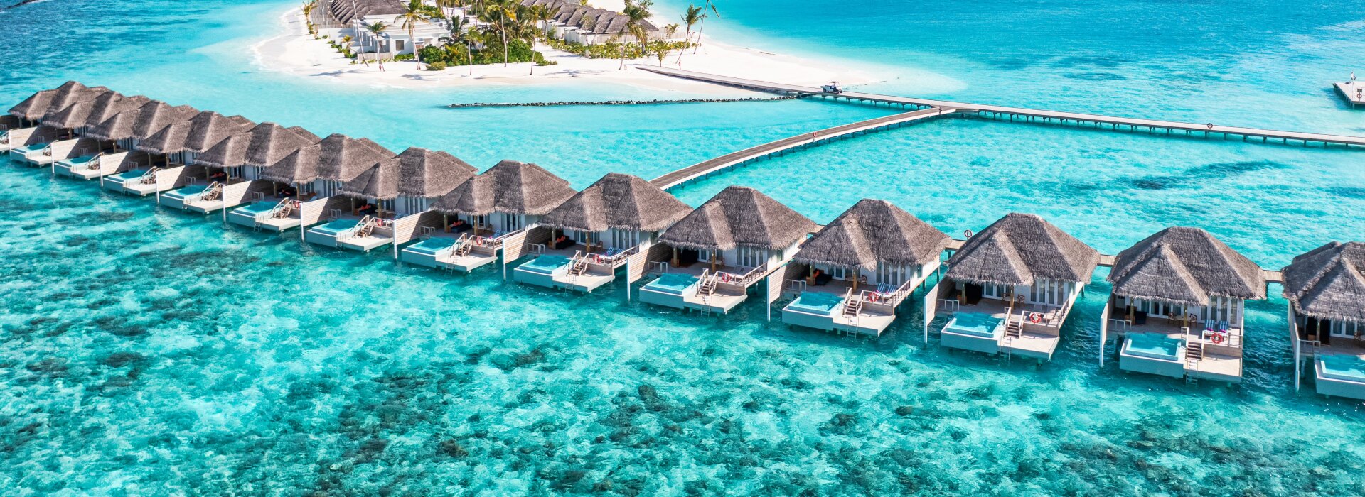 Splendida vista aerea di un resort tropicale con ville private sopra le acque turchesi dell'oceano.