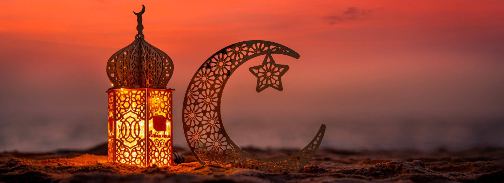 Lanterna decorativa di Ramadan e ornamento a forma di mezzaluna sulla spiaggia sabbiosa durante un tramonto arancione.