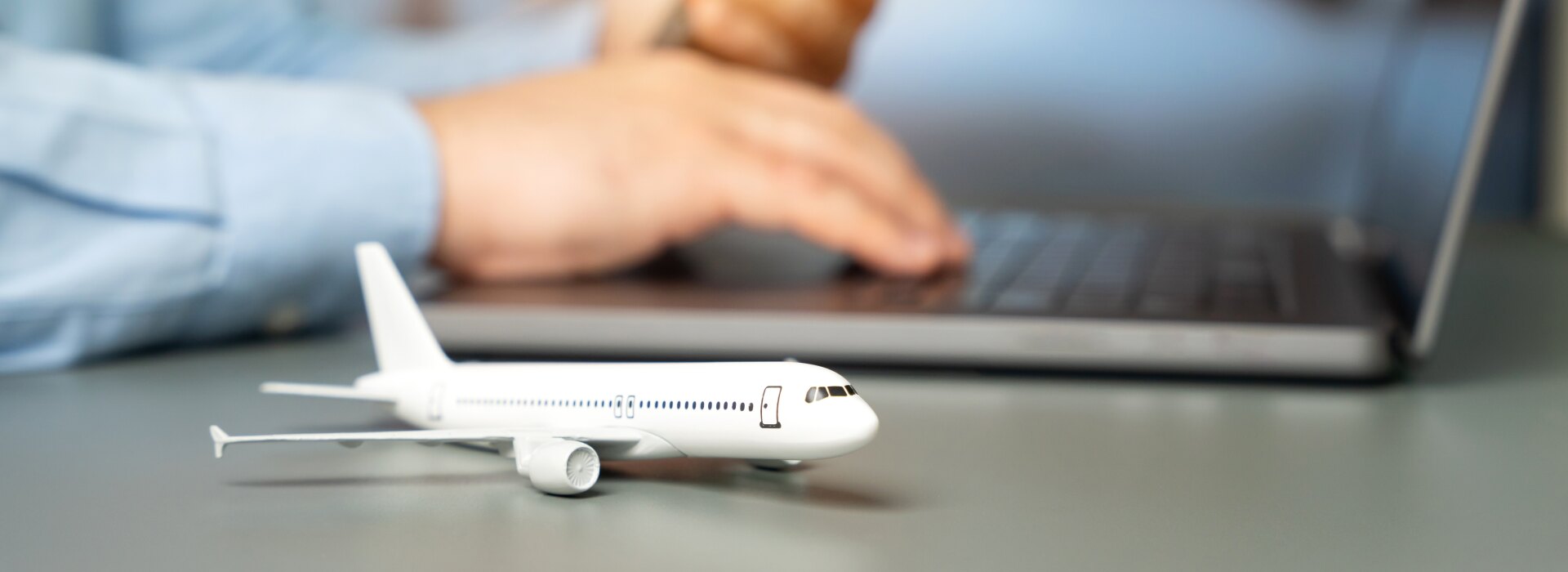 Close up of a person using a laptop and smartphone to book a flight with a miniature airplane model on the desk.